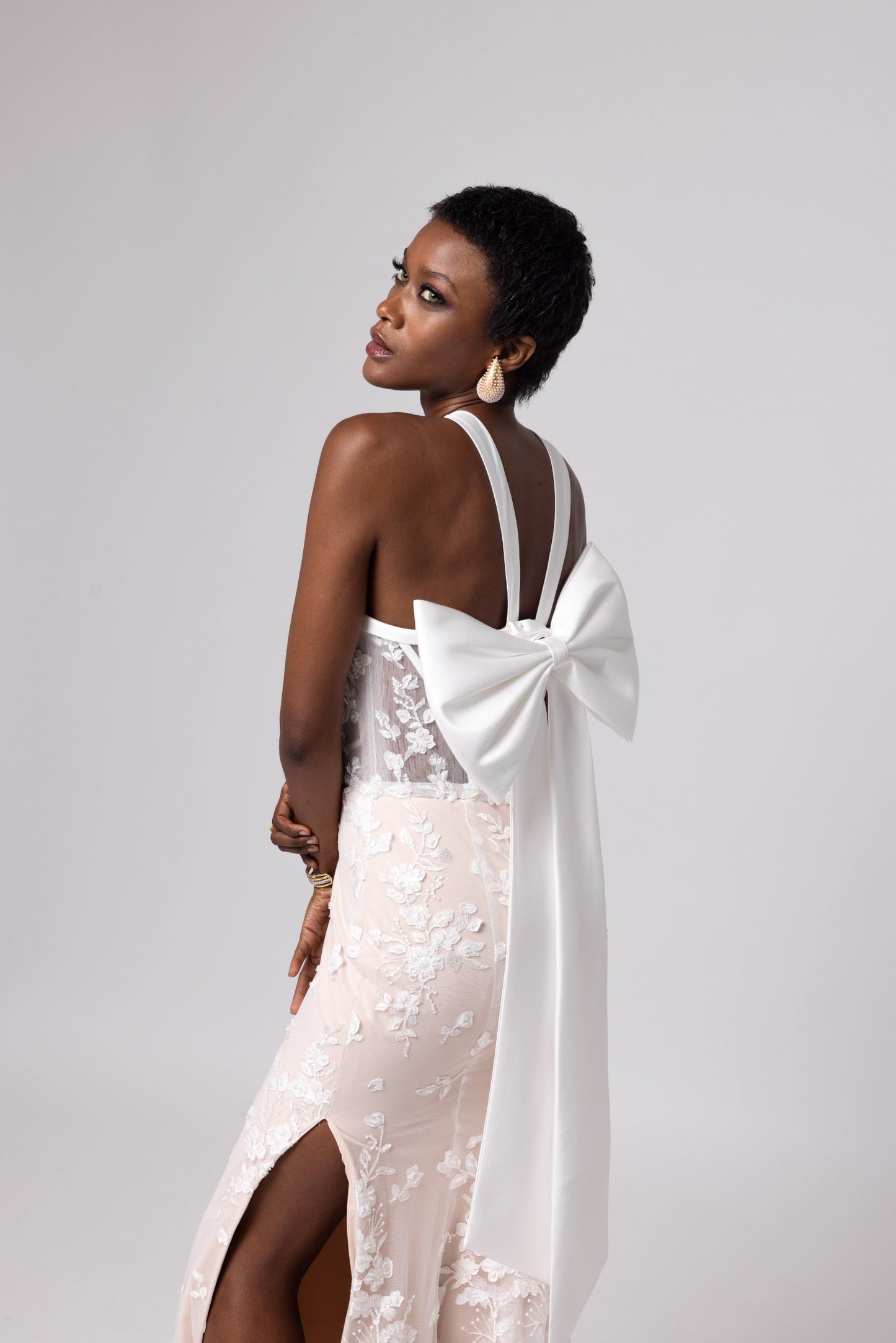 Nude underlay lace gown, white piping details, halter neckline with side slits. Large cascading bow in the back.