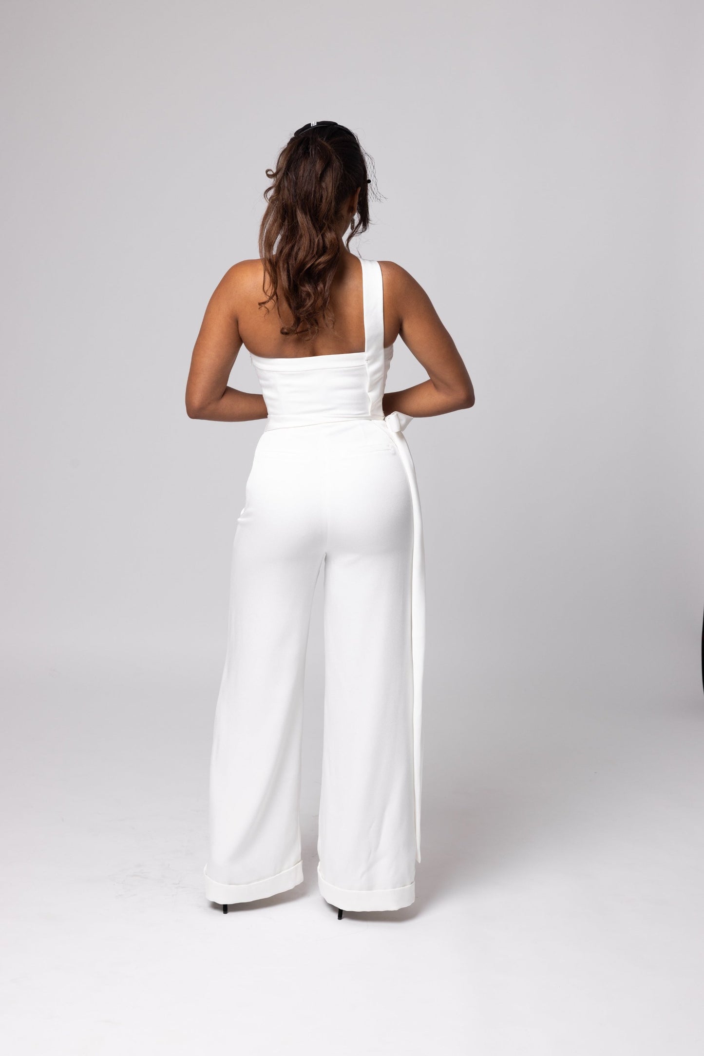 Off-white scoop neckline one shoulder jumpsuit. Long, side bow at waist, cuffed hemline.